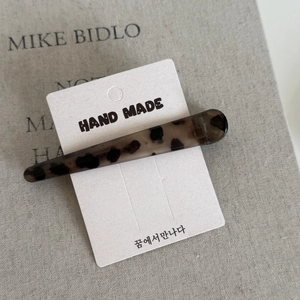 Detail shot of leopard print acrylic hair clip on packaging over a textured book