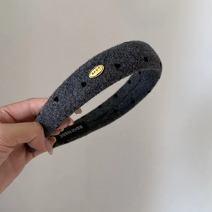 Détail d'un serre-tête en laine avec motifs de cœurs et plaque en métal doré 'Love'