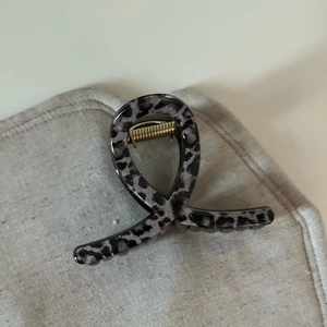 Detail of grey leopard print hair claw clip with golden spring on textured fabric