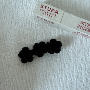 Detailed macro view of black crocheted triple flower hair clip on soft fabric background