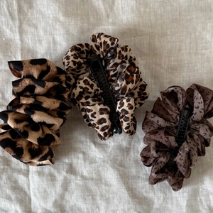 Three leopard print scrunchie banana hair clips in assorted brown tones on white fabric