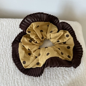 Detail of yellow polka dot scrunchie with brown pleated mesh trim on white fabric