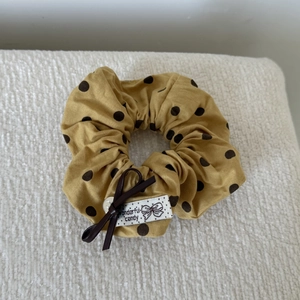 Close-up of yellow polka dot scrunchie with brown bow and white fabric label detail