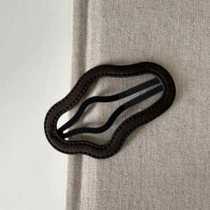 Detail view of wavy coffee brown fabric hair clip with textured stitching on beige cotton