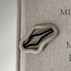 Minimalist wavy fabric hair clip in beige color shown on a textured linen background