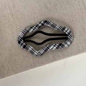 Detail of wave-shaped BB clip featuring black and white plaid fabric on a metal base