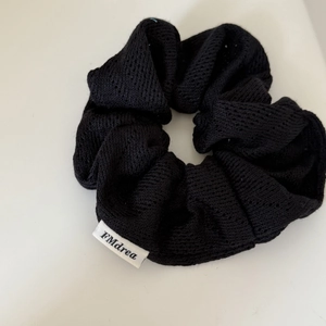 Detail showing the knitted texture and white logo tag on the black scrunchie