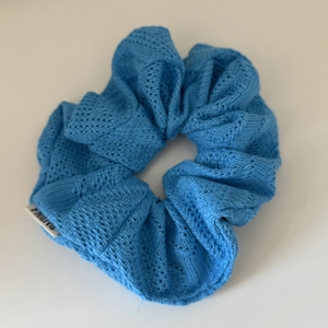 Detail of light blue knitted scrunchie showing hollow knit pattern and brand label