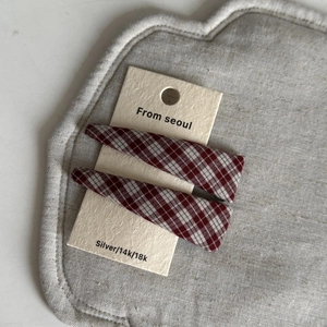 Close-up of two red plaid fabric hair clips neatly arranged on a branded display card