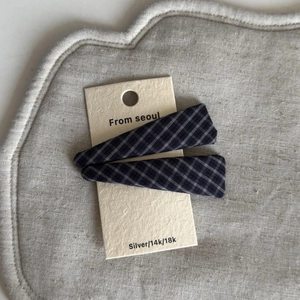Detail of two plaid pattern hair clips in dark blue fabric on a neutral card base
