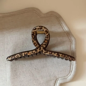 Large leopard print hair claw clip with strong gold spring on minimalist beige background