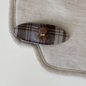 Détail d'une pince à cheveux à carreaux marron avec un petit ours floqué et nœud doré