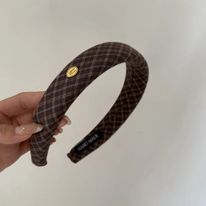 Macro view of brown plaid headband with golden metal tag and handmade fabric label