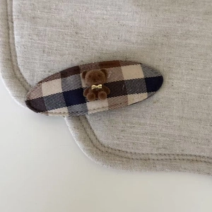 Détail d'une barrette à cheveux à carreaux avec petit ours brun et nœud doré