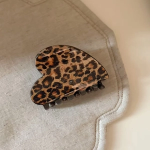 Macro shot of heart-shaped leopard print hair claw clip on beige linen background