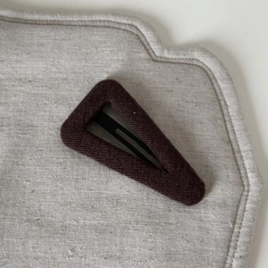 Detailed top view of ribbed knit fabric bb hair clip in deep burgundy on grey textured base