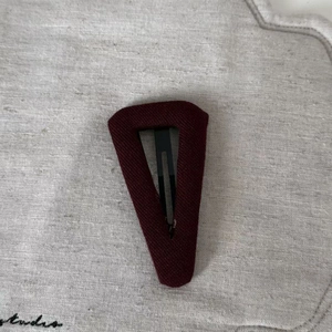 Close-up of deep red knitted fabric BB hair clip with detailed stitch texture on grey surface