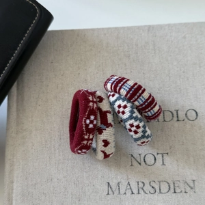 Detail of four knitted hair ties with festive elk and stripe patterns on a textured book