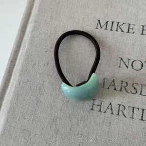 Minimalist geometric crescent acetate hair tie with brown elastic rope on a gray book