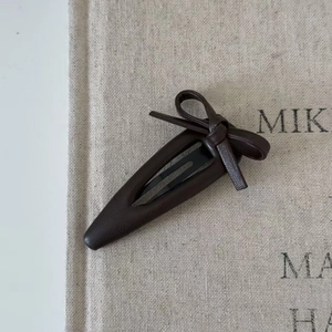 Deep brown faux leather bow hair clip with black metal BB clip on retro fabric background