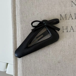 Close-up of a black leather bow hair clip on a textured beige fabric background