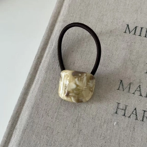 Close-up of cream marble resin charm on a dark brown elastic hair tie against a book