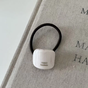 Detail of a black elastic hair tie featuring a white square charm with France Handmade text