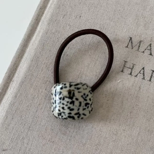 Close-up of a brown elastic hair tie with a spotted black and white acetate bead detail
