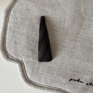 Vintage triangular hair clip with brown and blue-grey stripes on a beige fabric background
