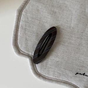 Vintage oval fabric snap hair clip with brown and blue stripes on a linen mat