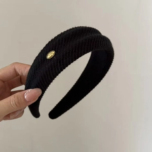 Close-up of black knitted headband with diagonal texture and gold-tone Love emblem