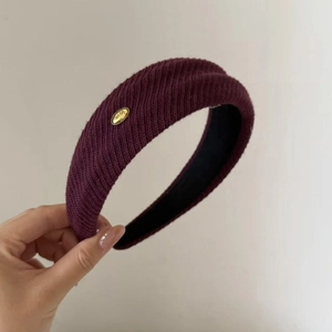 Detail of burgundy knitted headband with a gold-tone LOVE metal tag and ribbed texture