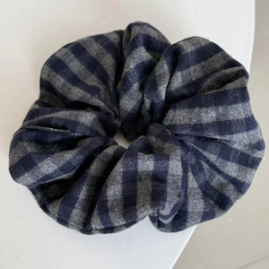 Detail view of navy blue and grey plaid fabric scrunchie with twill texture and brand tag