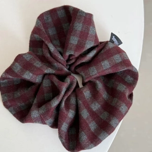 Detailed view of red and grey plaid scrunchie with soft fabric and branded woven label