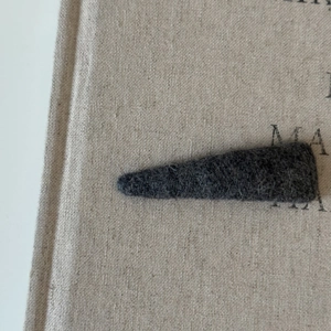 Macro view of dark grey felt fabric texture on triangle hair clip with beige burlap background