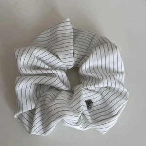 Detail of navy blue striped scrunchie with a black heart bead on a white background