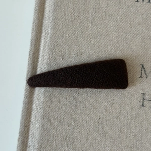 Close-up of a dark brown knit fabric covered triangular BB hair clip on beige linen