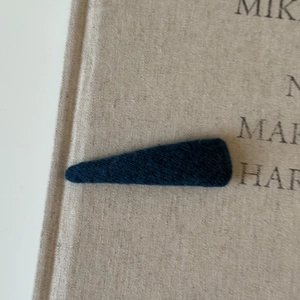 Close-up of deep cyan fabric hair clip resting on a textured linen book cover