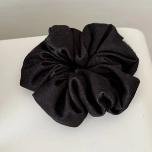 Close-up of black fabric scrunchie with fine twill texture and small brand label tag