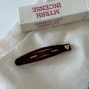 Detail of burgundy velvet hair clip with a golden metal heart on a linen background