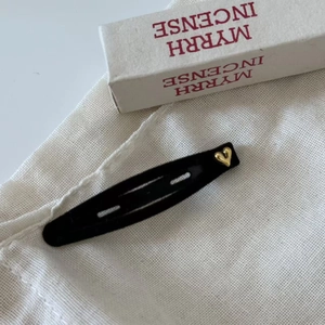 Elegant black velvet BB hair clip with golden heart detail on a textured white fabric