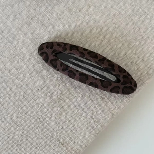 Detailed close-up of a leopard print knitted hair clip on a textured fabric background