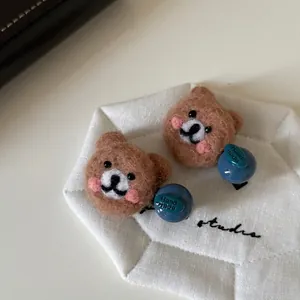 Pair of handmade brown wool felt bear hair clips with blue beads on a white tray