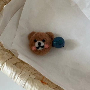 Detailed macro view of a handmade brown wool felt bear hair clip with a blue plastic clasp