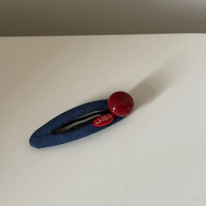 Close-up of a blue denim BB hair clip with red resin bead and Korean branding element