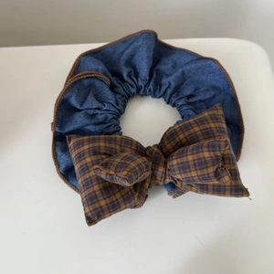 Close-up of denim blue checkered bow scrunchie with detailed brown stitched edges