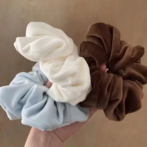 Three premium soft velvet scrunchies in cream, light blue and brown held by hand