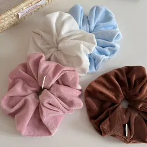 Set of soft velvet scrunchies in white, blue, pink, and brown on a minimalist surface