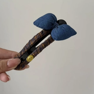 Detail of denim bow hair clip featuring a plaid fabric base and gold Korea logo badge