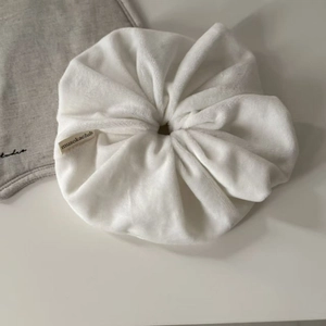 Close-up of soft white velvet scrunchie with brand label on minimalist linen background